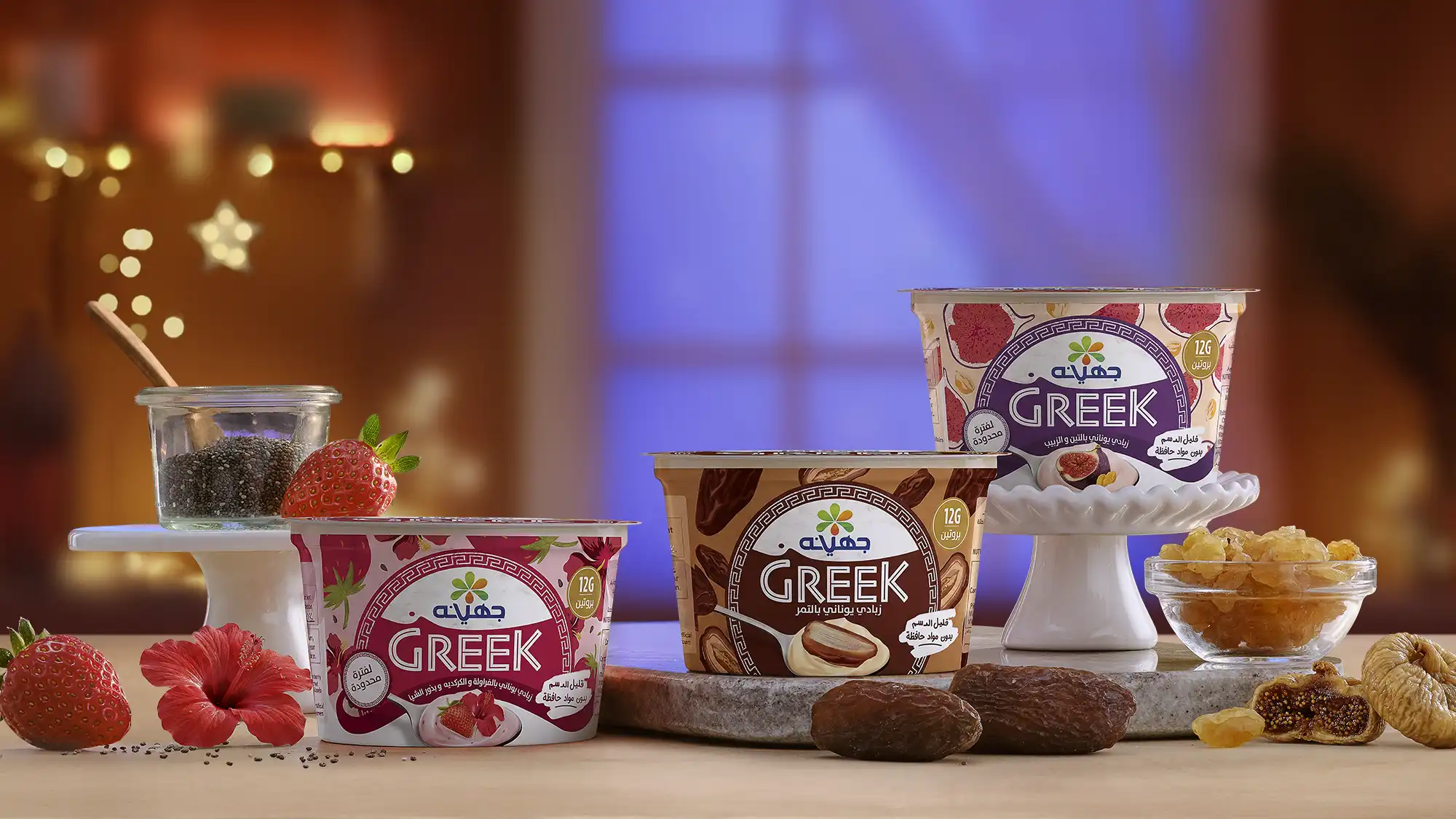 Food Photography © Mechanix Studios Juhayna Greek yogurt cups in three limited-edition flavors — Strawberry Hibiscus & Chia, Dates, and Fig & Raisins — displayed on a warm-lit surface with fresh fruit, dates, and golden raisin garnishes