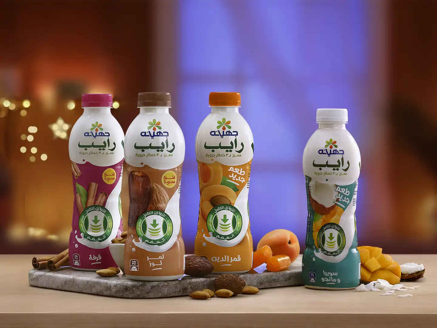 Food photography © mechanix studios Juhayna Rayeb probiotic yogurt drink in four flavors — Cinnamon, Dates & Almonds, Qamar El-Din (Apricot), and Soobia & Mango — arranged on a marble slab with Ramadan bokeh lighting and natural ingredient props